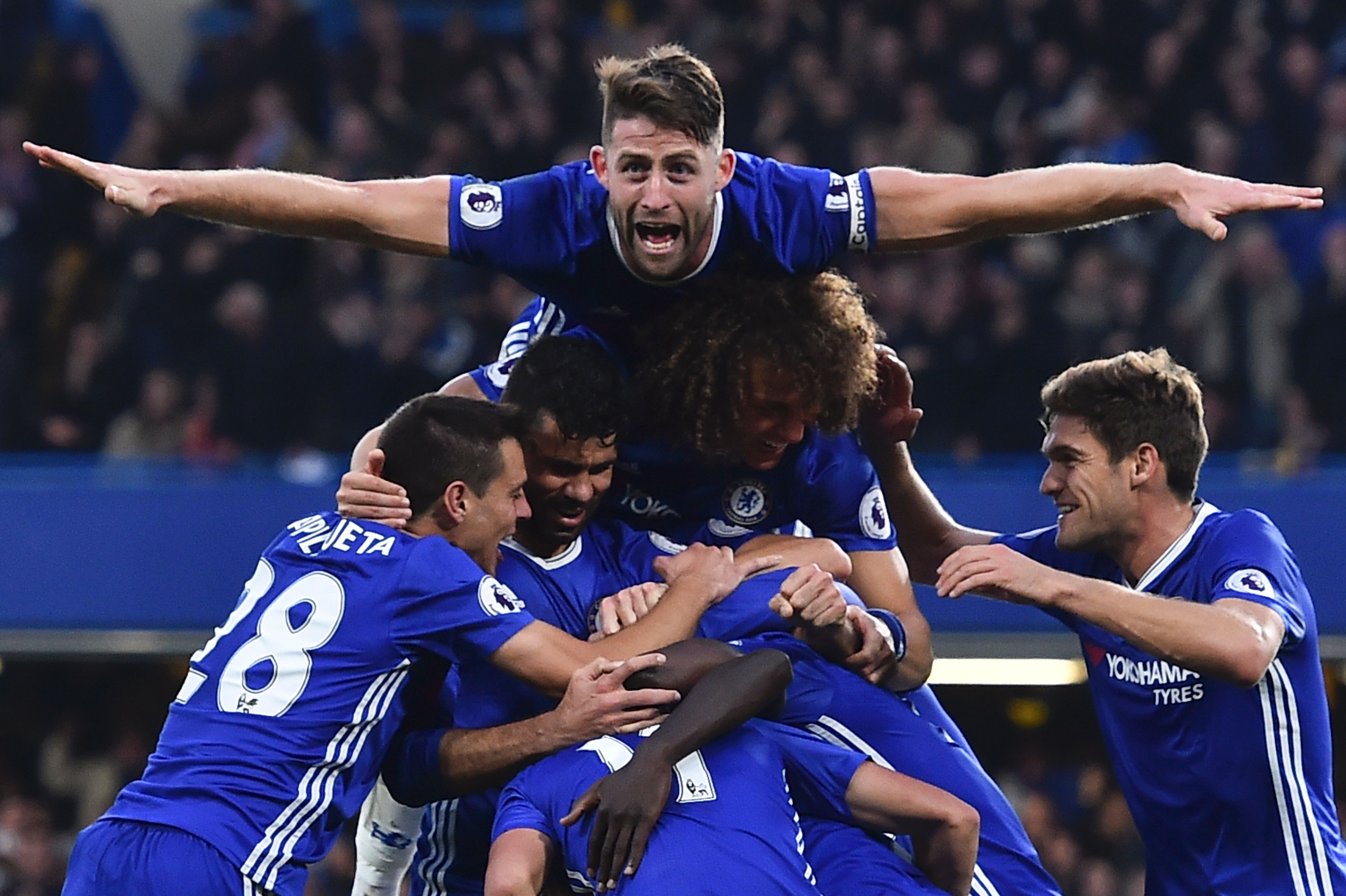 Chelsea's English defender Gary Cahill (top) jumps onto the huddle to join the celebrates after Chelsea's French midfielder N'Golo Kante scored their fourth goal during the English Premier League football match between Chelsea and Manchester United at Stamford Bridge in London on October 23, 2016. / AFP / GLYN KIRK / RESTRICTED TO EDITORIAL USE. No use with unauthorized audio, video, data, fixture lists, club/league logos or 'live' services. Online in-match use limited to 75 images, no video emulation. No use in betting, games or single club/league/player publications. / (Photo credit should read GLYN KIRK/AFP/Getty Images)