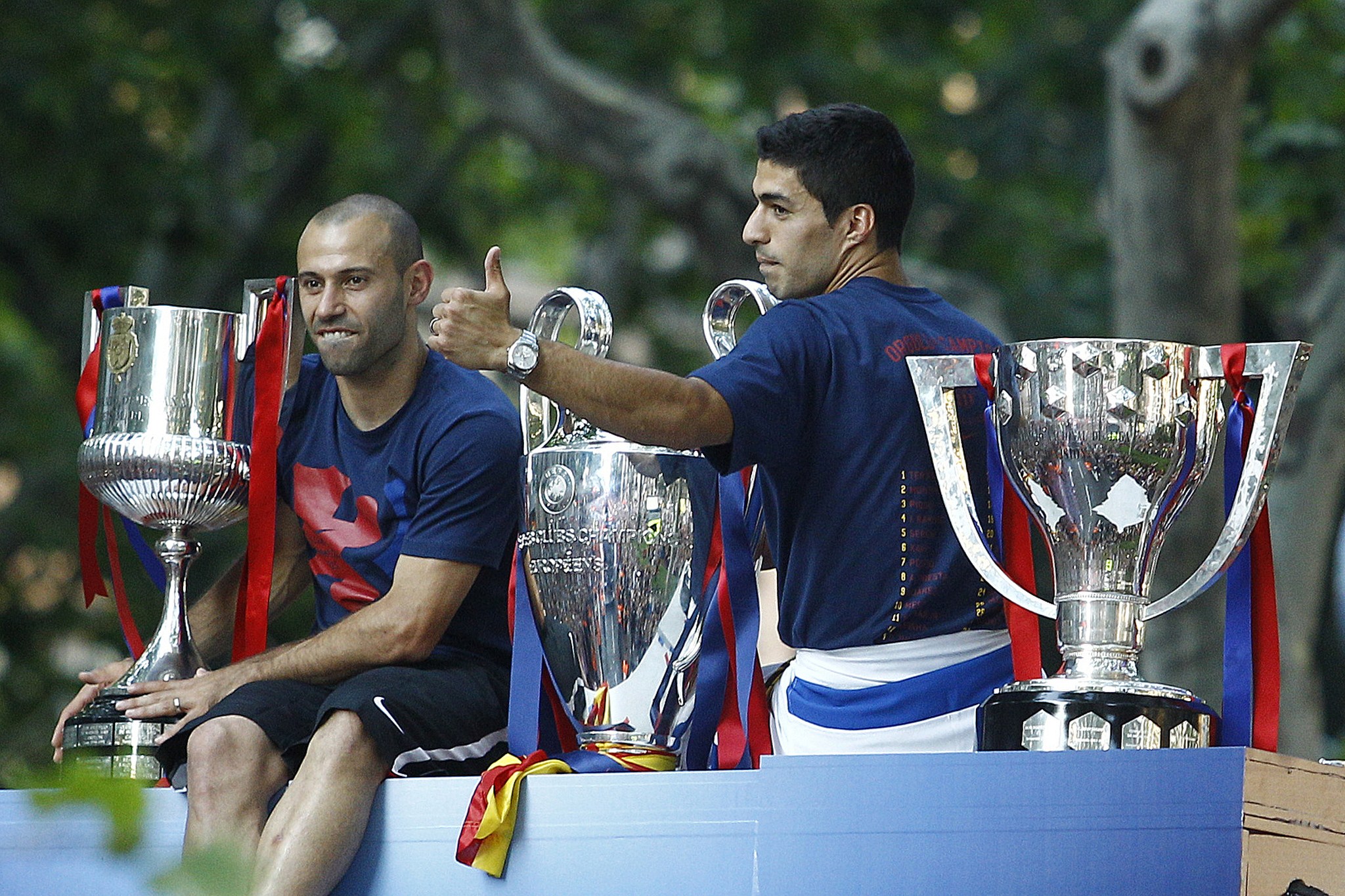 Barcelona's Uruguayan forward Luis Suarez (R) and  Barcelona's Argentinian defender Javier Mascherano pose with the three trophies on a bus parading through the streets of Barcelona as the team celebrate its victory over Juventus one day after the UEFA Champions League final football on June 7, 2015. Luis Suarez and Neymar scored second-half goals to give Barcelona a 3-1 Champions League final victory over Juventus on June 6, 2015 as the Spaniards became the first team to twice win the European treble.   AFP PHOTO/ QUIQUE GARCIA        (Photo credit should read QUIQUE GARCIA/AFP/Getty Images)