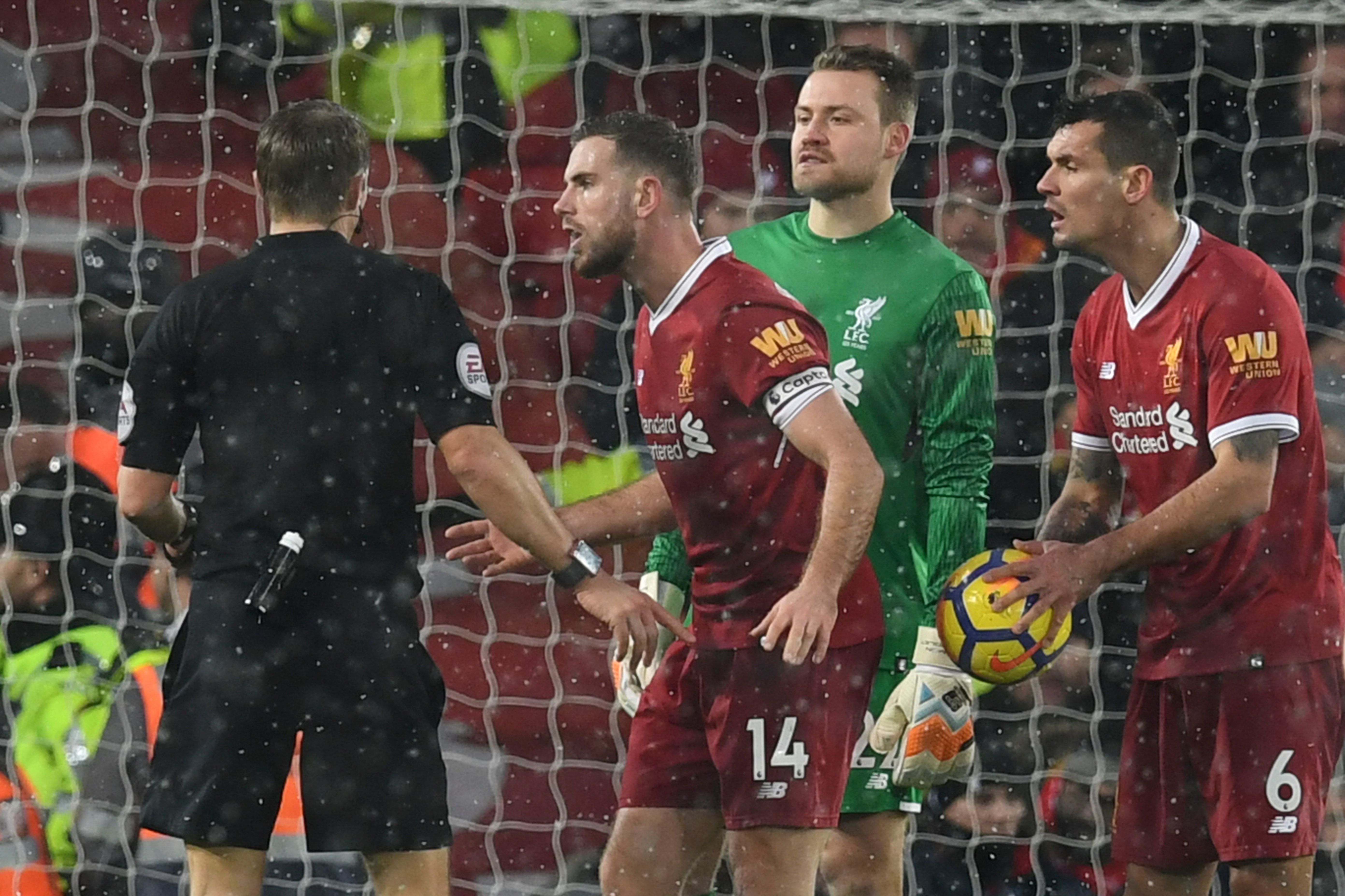Liverpool's English midfielder Jordan Henderson (C) and Liverpool's Croatian defender Dejan Lovren (R) talk with referee Craig Pawson (L) after Lovren conceded a penalty during the English Premier League football match between Liverpool and Everton at Anfield in Liverpool, north west England on December 10, 2017.  / AFP PHOTO / Paul ELLIS / RESTRICTED TO EDITORIAL USE. No use with unauthorized audio, video, data, fixture lists, club/league logos or 'live' services. Online in-match use limited to 75 images, no video emulation. No use in betting, games or single club/league/player publications.  /         (Photo credit should read PAUL ELLIS/AFP/Getty Images)