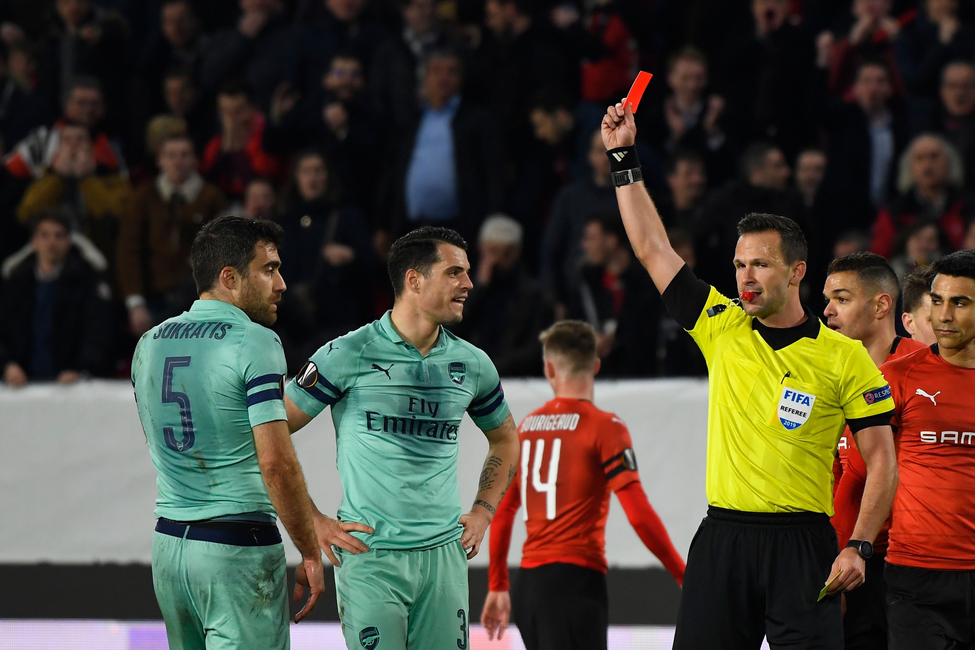 Slovak referee Ivan Kruzliak (R) shows a red card to Arsenal's Greek defender Sokratis Papastathopoulos (L) during the UEFA Europa League round of 16 first leg football match between Stade Rennais FC and Arsenal FC at the Roazhon Park stadium in Rennes, northwestern France on March 7, 2019. (Photo by DAMIEN MEYER / AFP) (Photo credit should read DAMIEN MEYER/AFP/Getty Images)