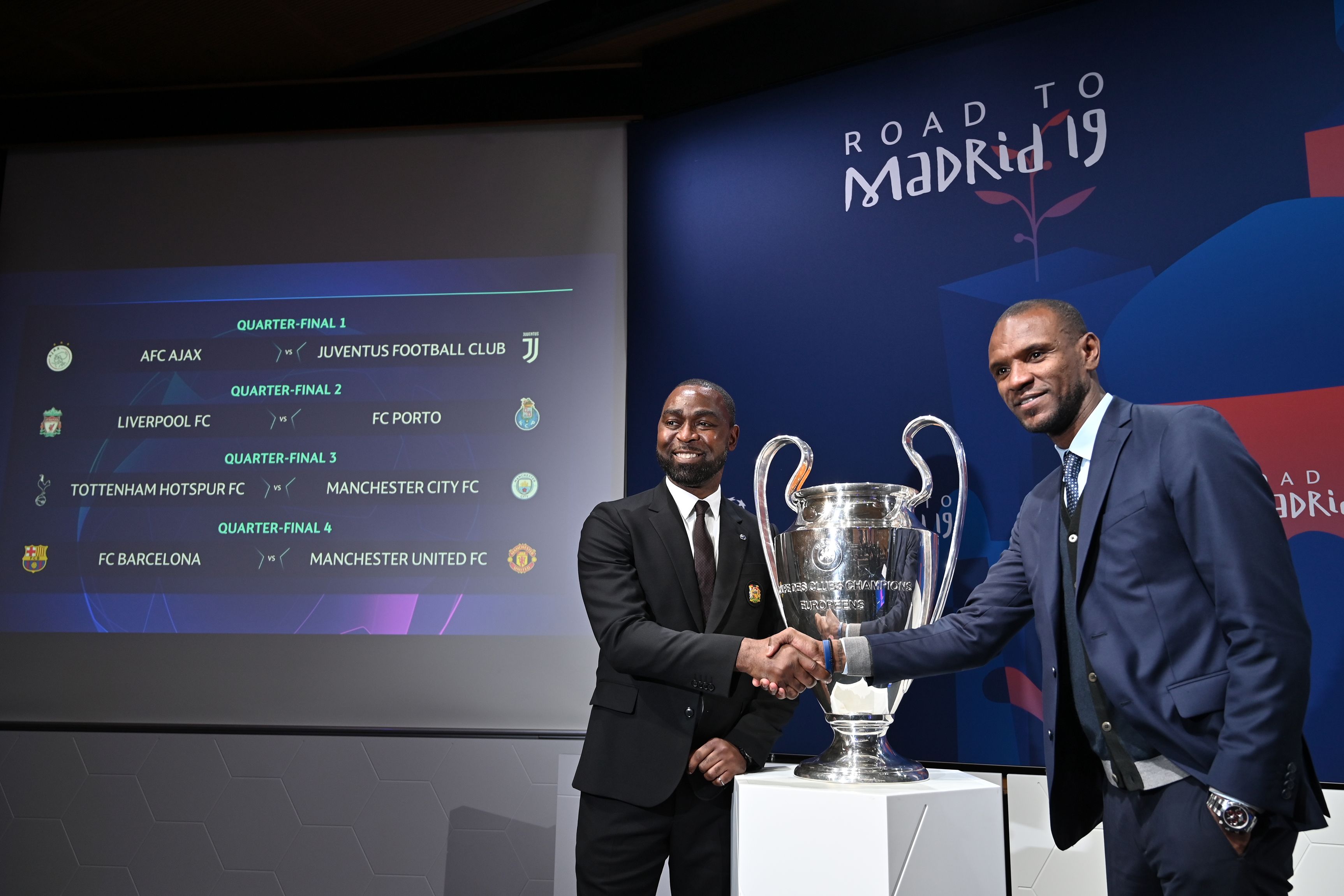 Manchester United football club ambassador Andy Cole (RL shakes hands with FC Barcelona ambassador Eric Abidal next to results of the draw for the Champions league quarter-final and the competition's trophy, on March 15, 2019 in Nyon. (Photo by Fabrice COFFRINI / AFP) (Photo credit should read FABRICE COFFRINI/AFP/Getty Images)